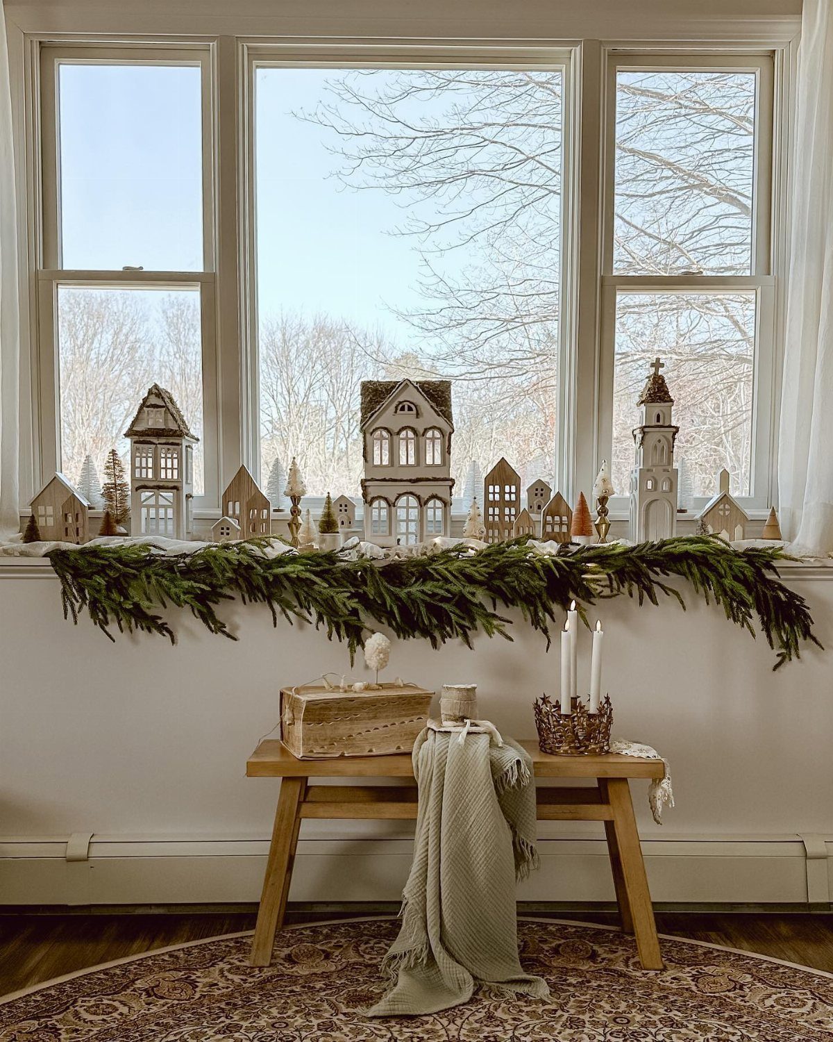 Green garland decorated with miniature wooden houses sitting on a wide windowsill.