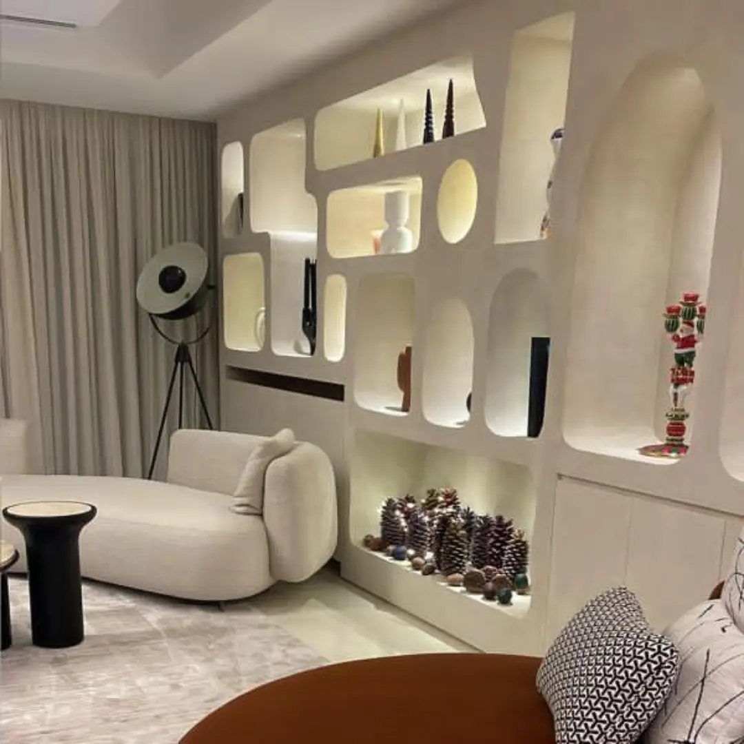 Sculptural built-in wall unit with organic recessed niches displaying various decorative objects in a modern living room.