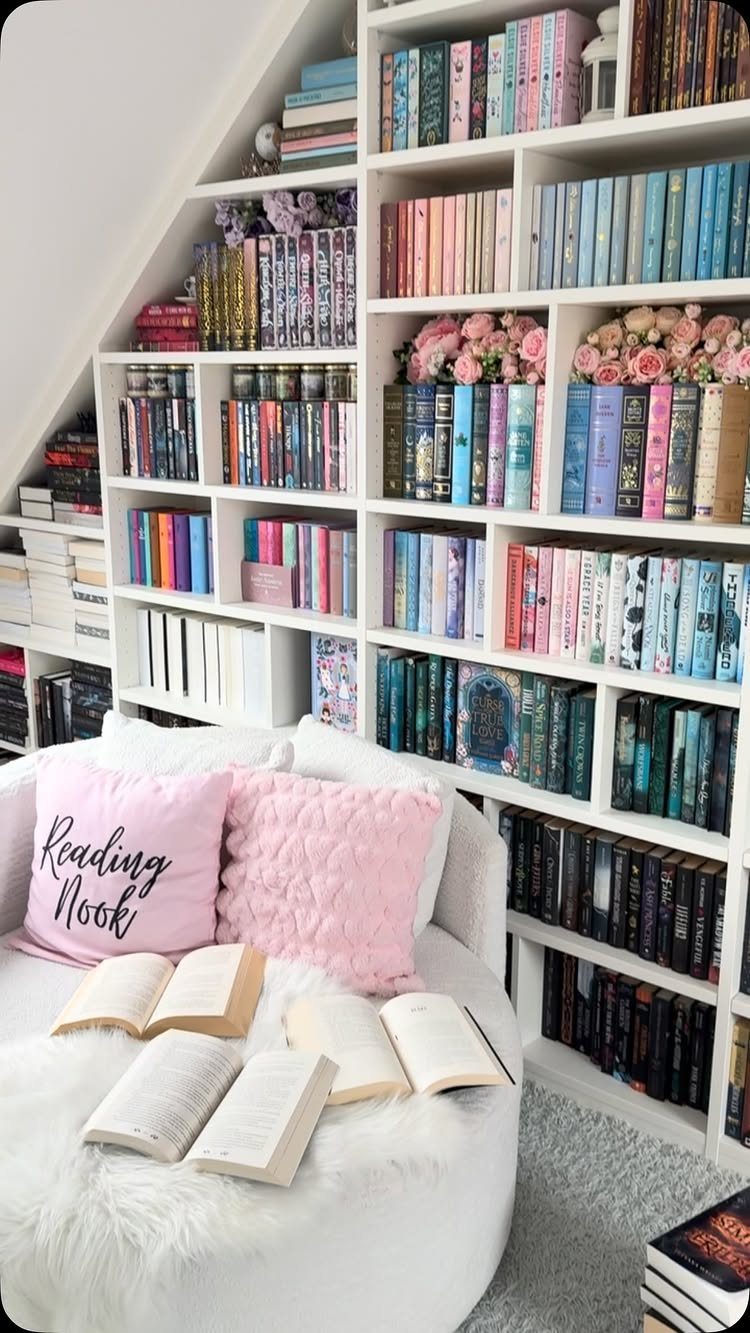 White bookshelves filled with colorful books and pink flowers next to a cozy armchair.