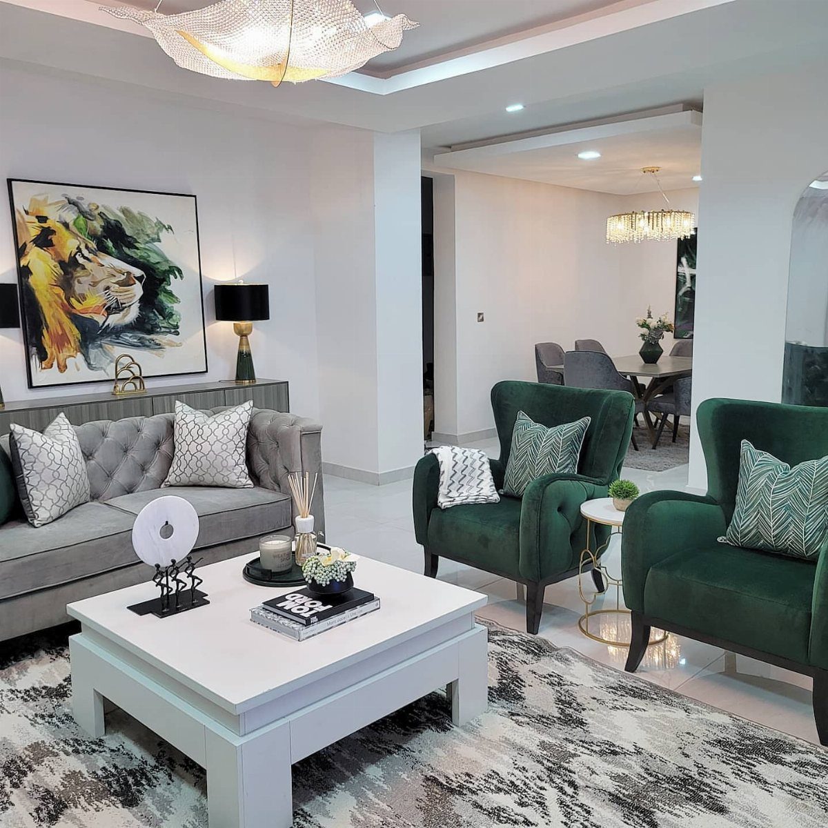 Modern living room with green velvet armchairs, grey sofa, and large tiger artwork on the wall.
