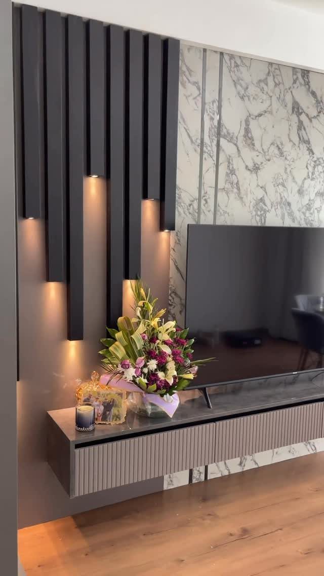 Black vertical wall slats with integrated warm LED lighting next to a marble wall and television.