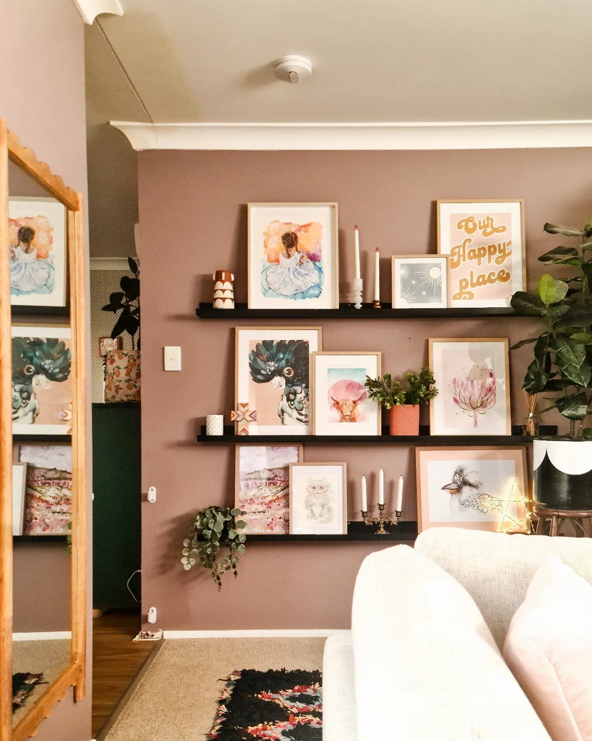 Black picture ledges on a mauve wall displaying various framed art prints and small decorative items.