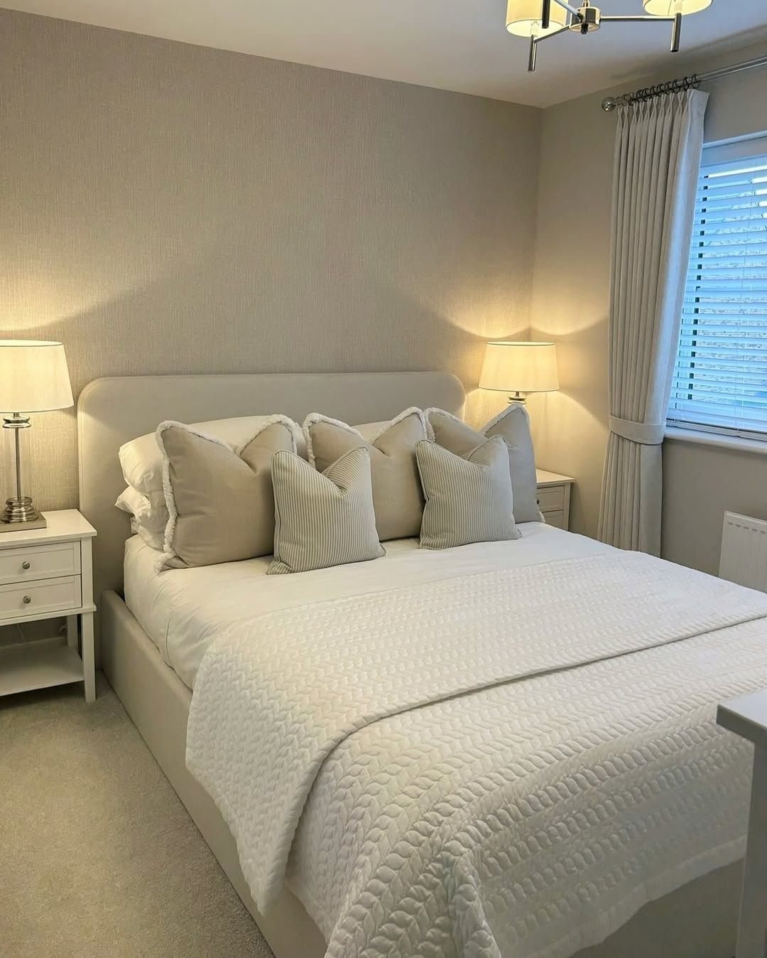 A white bed with plush cream pillows and quilted bedding in a neutral bedroom.