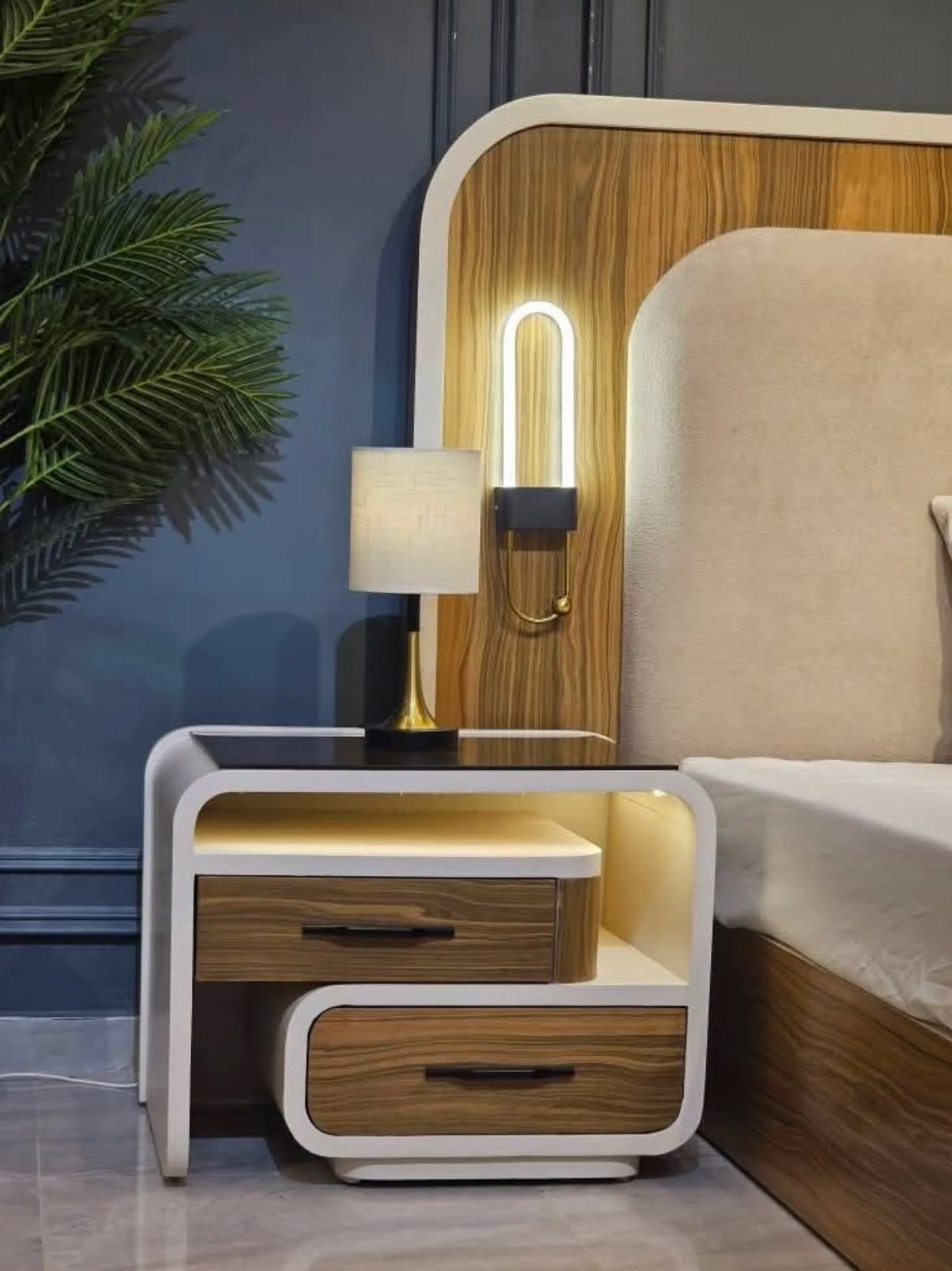 Modern white and wood bedside table with integrated lighting next to a bed.