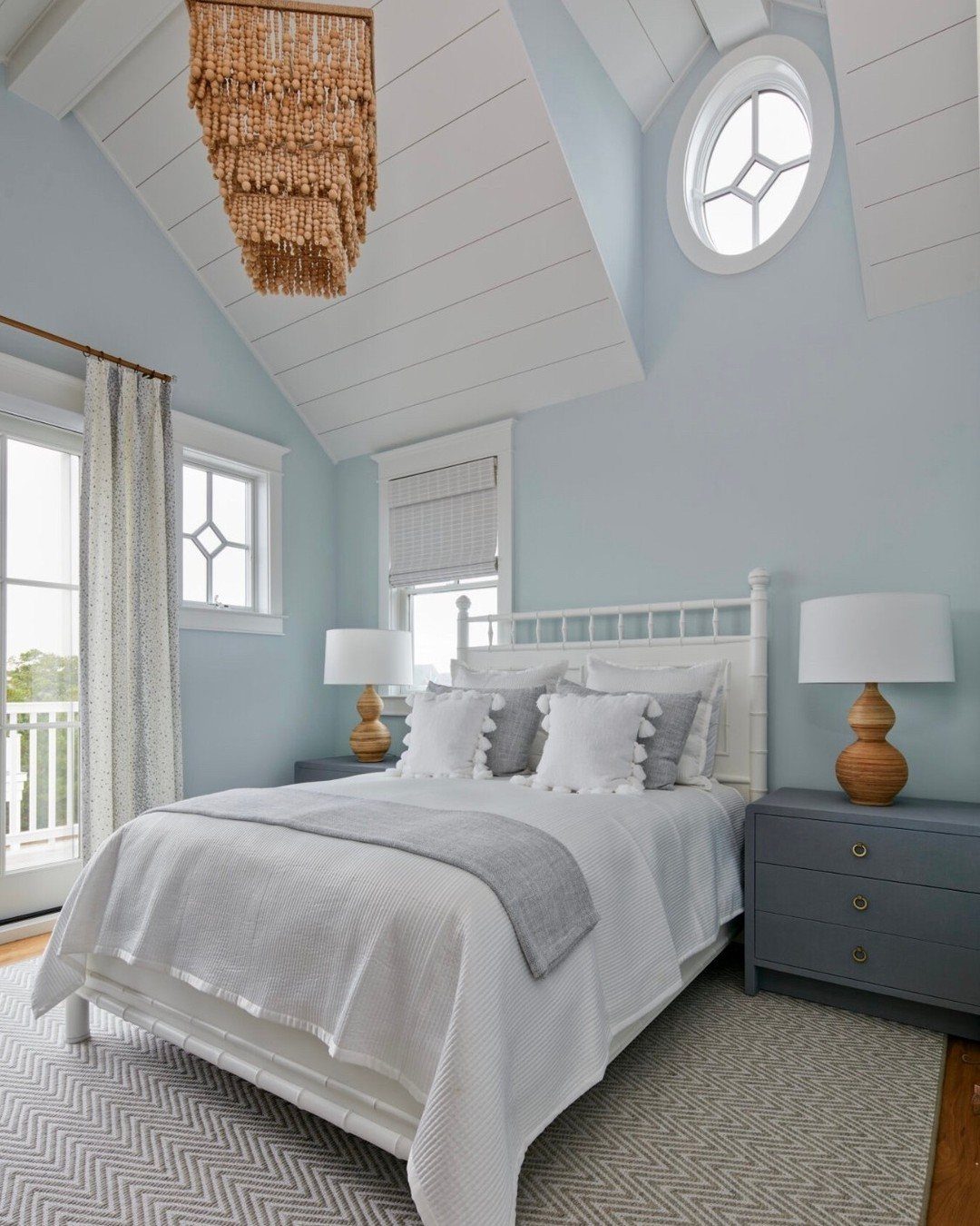 A serene light blue bedroom with white bedding, a beaded chandelier, and a patterned rug.