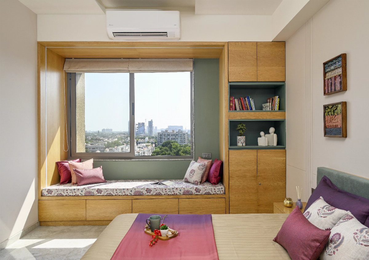 A built-in window seat with floral cushions and pink pillows overlooking a city skyline.
