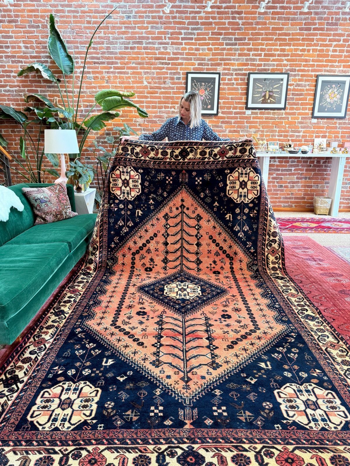 A woman displays a large navy and terracotta patterned vintage rug in a room with brick walls.