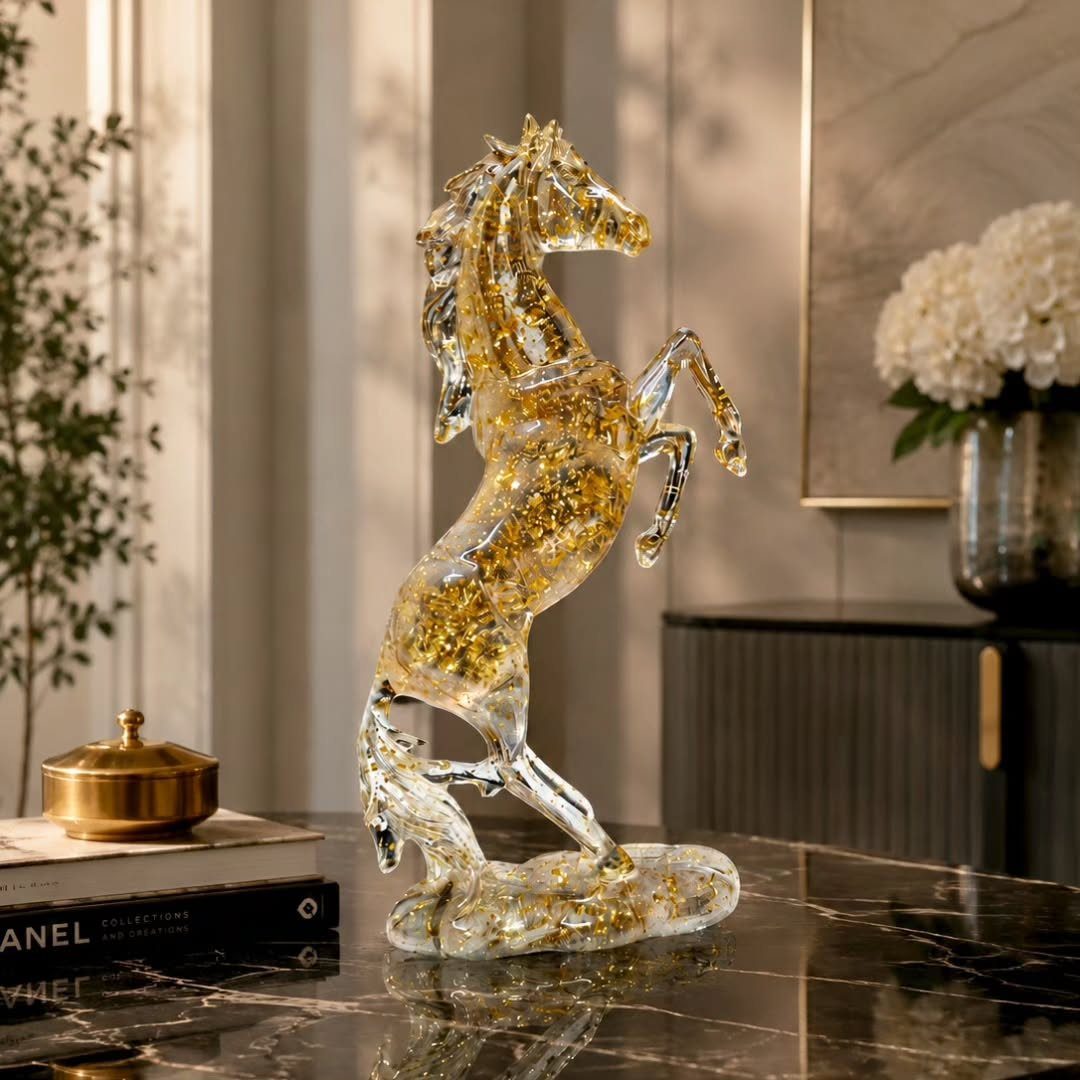 A gold-flecked glass horse sculpture standing on a black marble tabletop next to gold accessories.