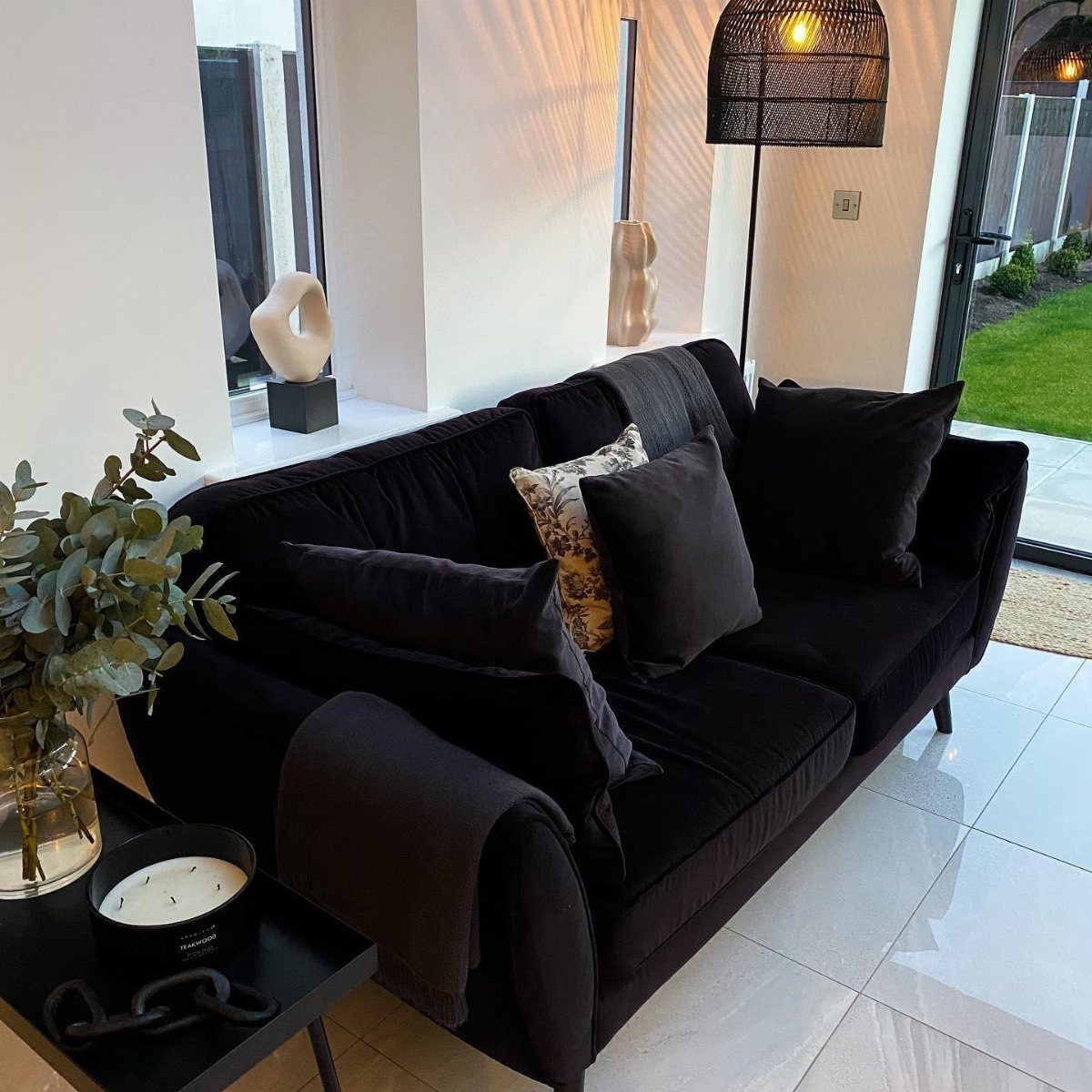 Black velvet sofa with decorative pillows in a bright, modern living room setting.