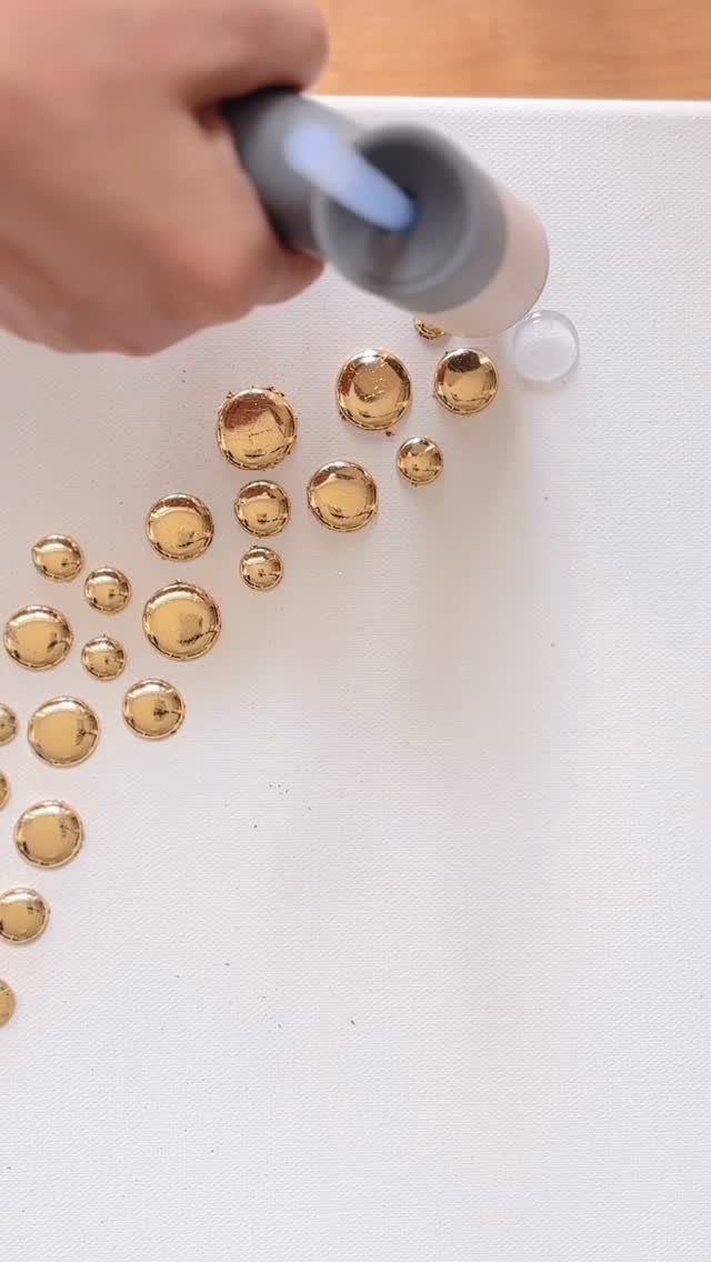 A hand applying glue to attach gold circular ornaments onto a white canvas surface.