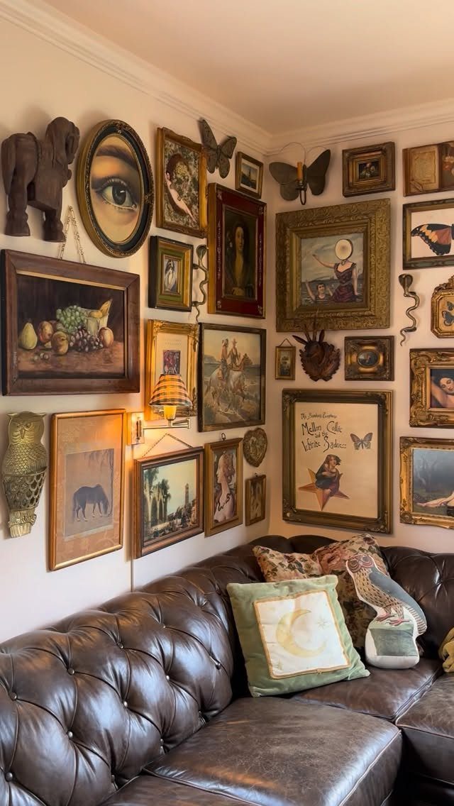 A large gallery wall filled with various gold and dark framed artworks above a leather sofa.