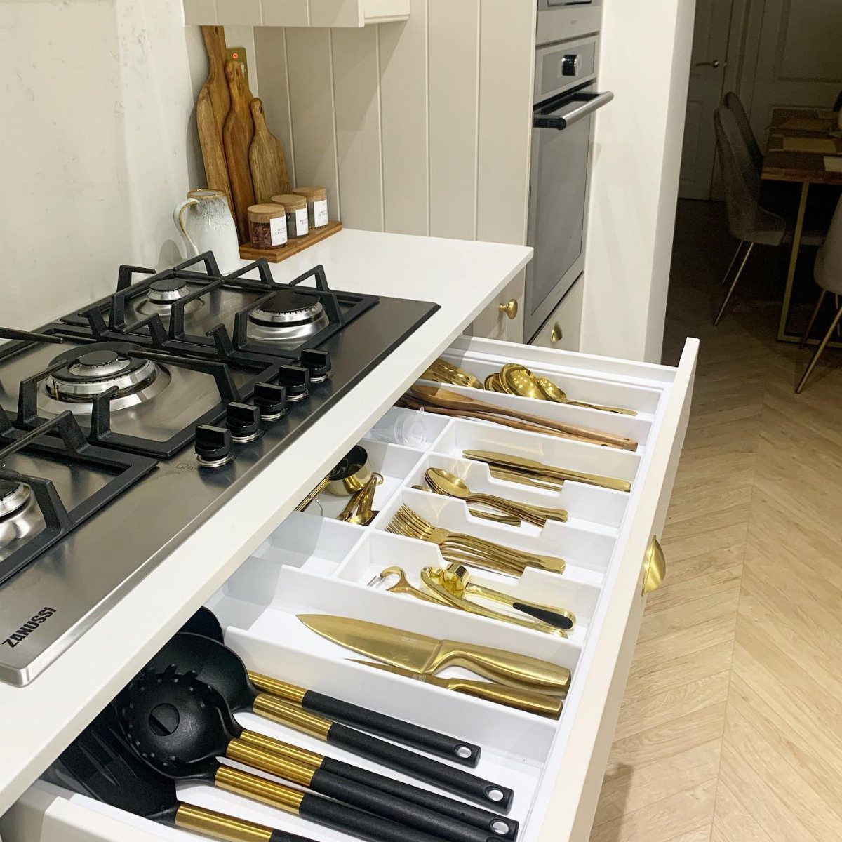 Gold and black kitchen utensils organized in a white drawer compartment system.