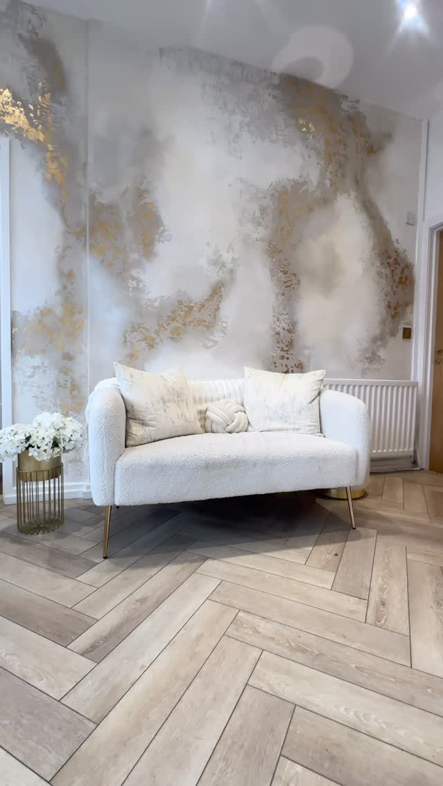 White textured wall with gold leaf accents behind a white loveseat and gold side table.