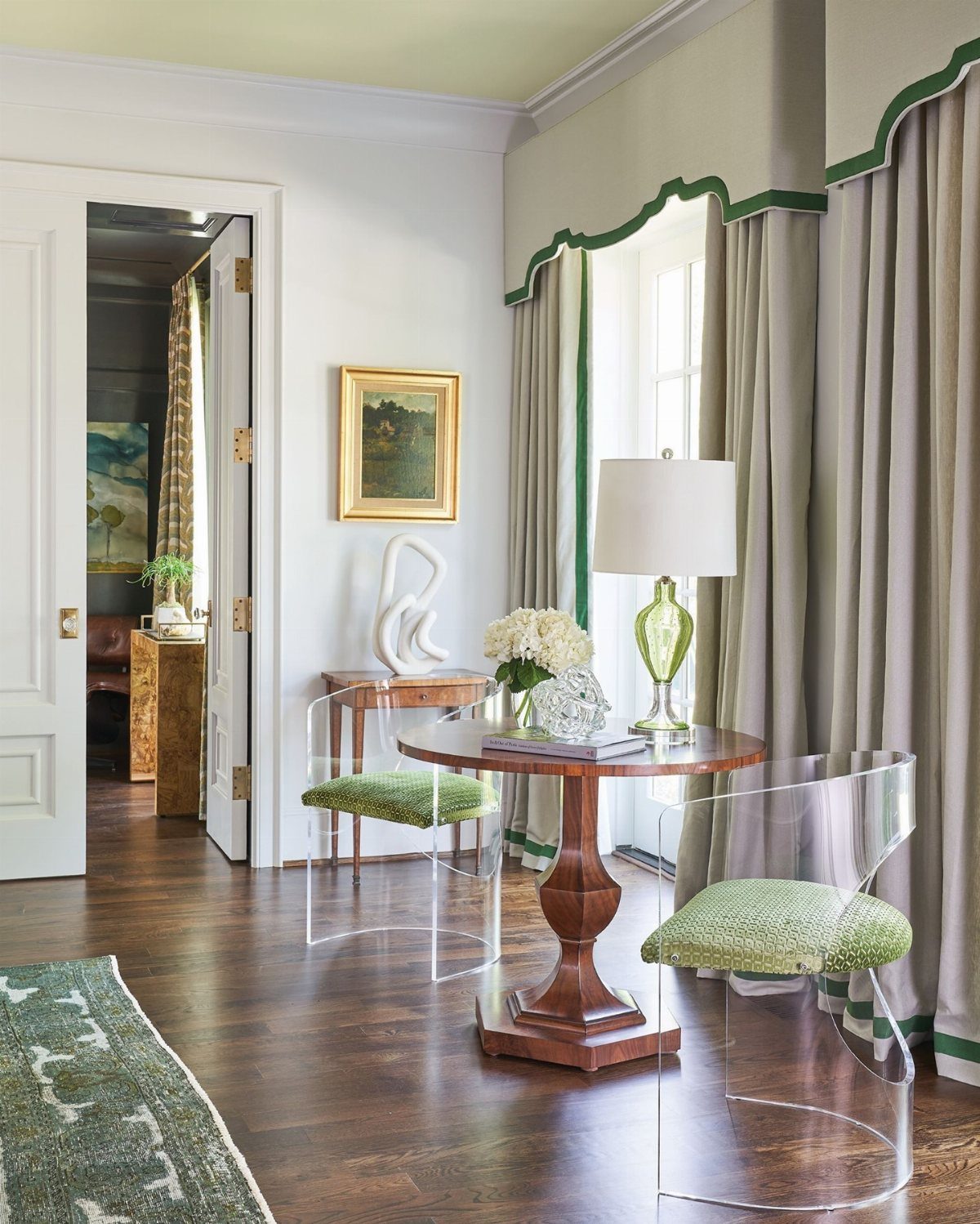 Clear acrylic chairs with green cushions around a small wooden table in a bright room.