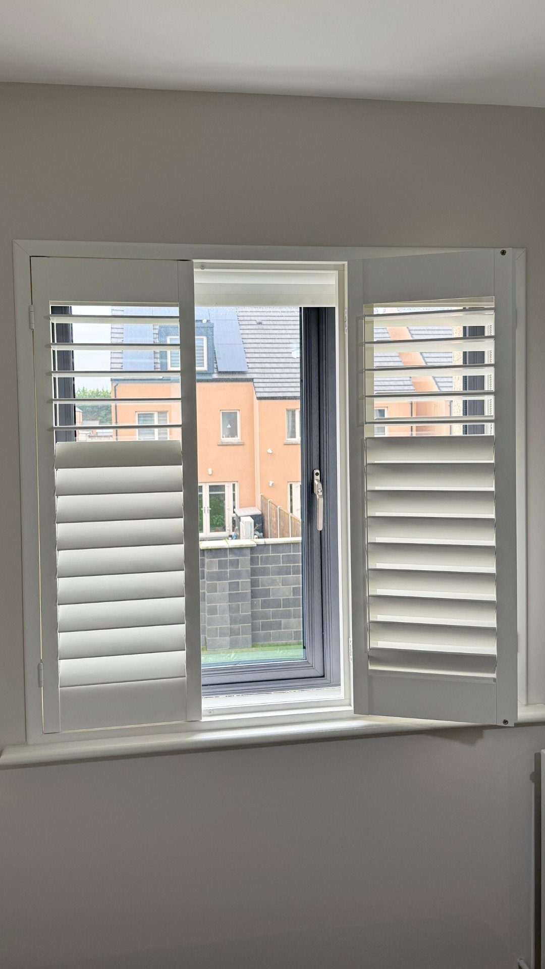 White plantation shutters installed on a window overlooking residential houses.