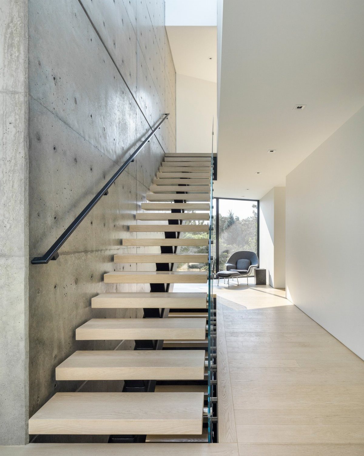 Modern floating wooden stairs against a textured concrete wall in a bright, minimalist hallway.