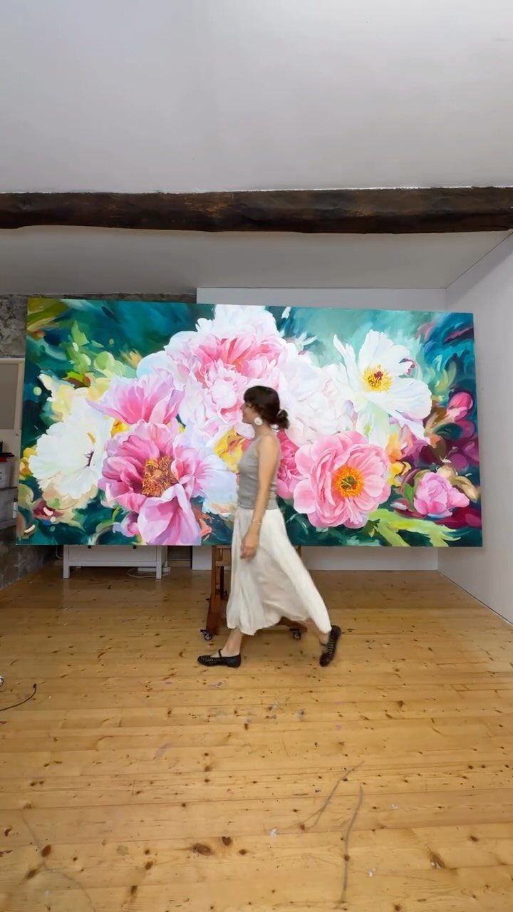 A woman walking past a massive floral painting with pink and white flowers.
