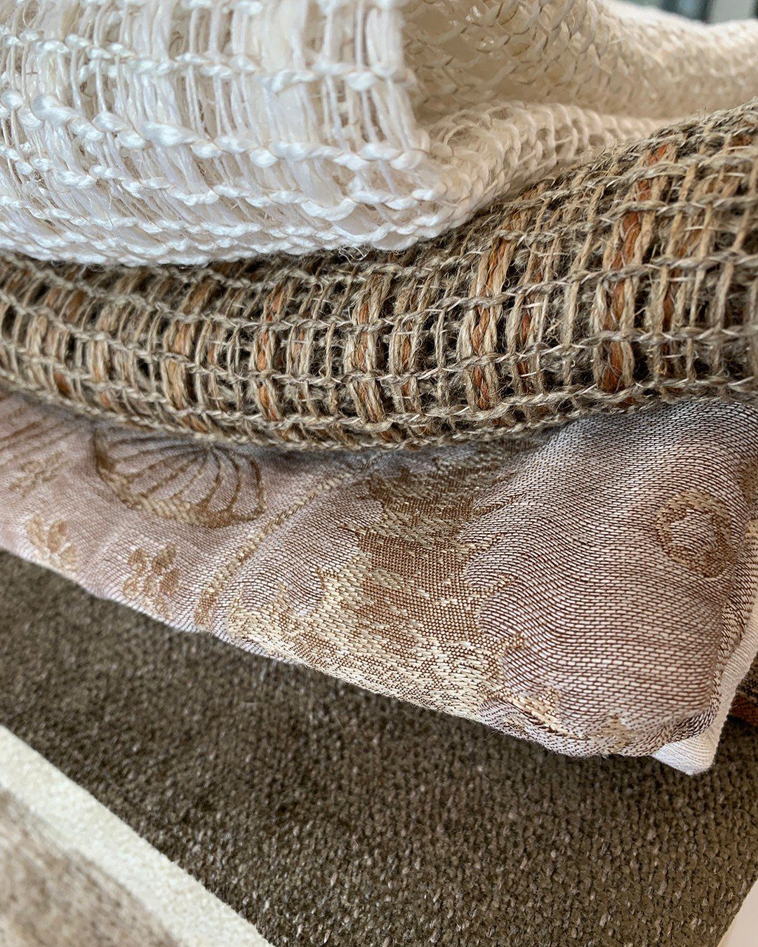 Close-up view of layered luxury textiles in white, brown, champagne, and olive green colors.