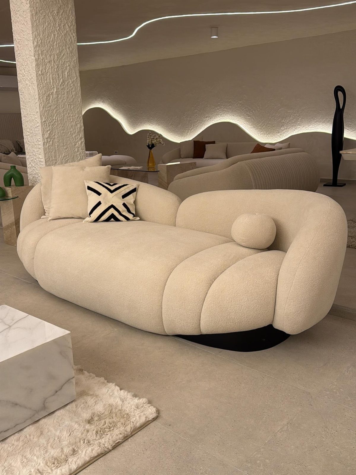 A large, cream-colored sculptural bouclé sofa with a patterned pillow in a minimalist room.