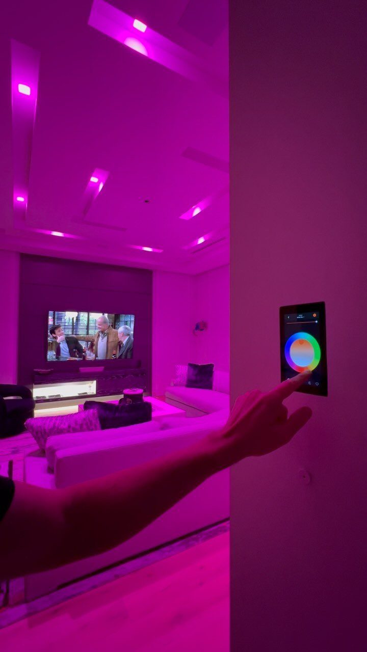 A hand interacting with a smart lighting control panel in a pink-lit living room.