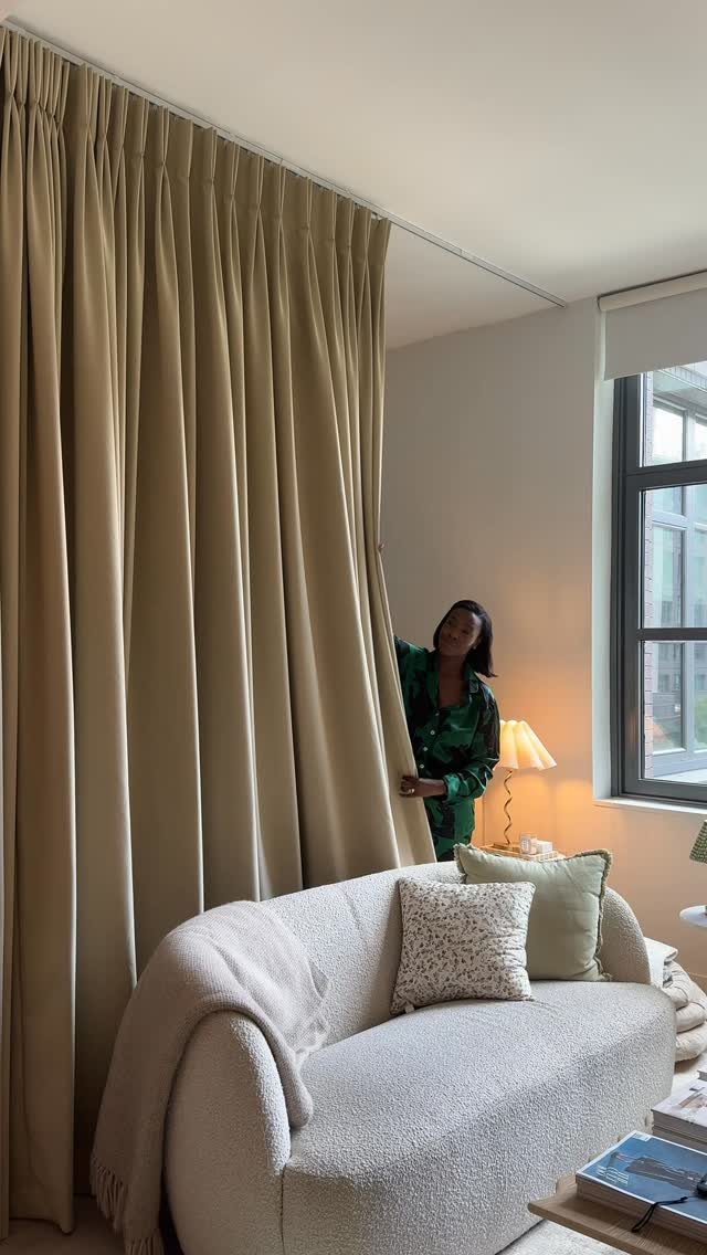 Beige floor-to-ceiling curtains hanging from a ceiling track in a modern living room.