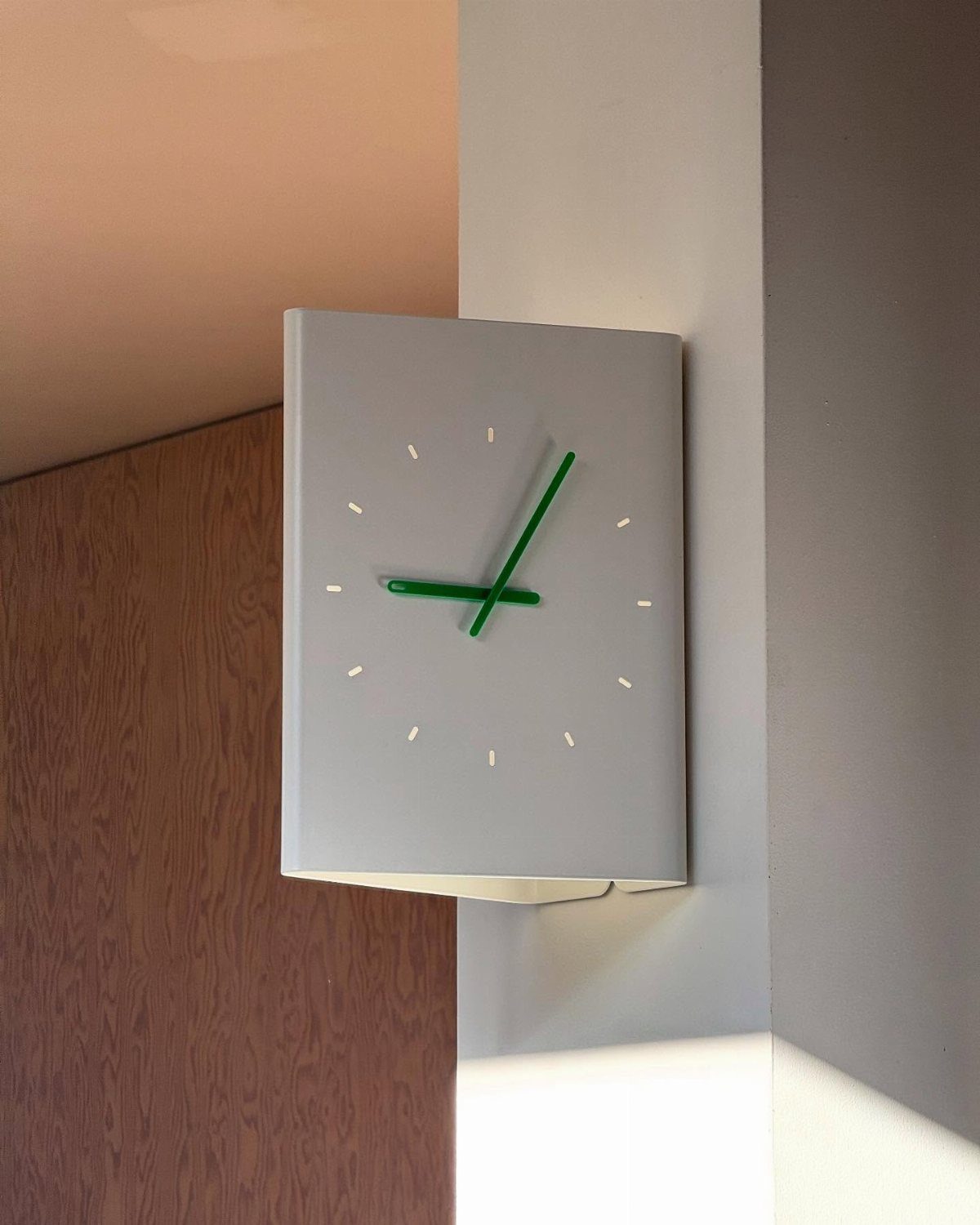 Large minimalist white wall clock with green hands mounted on a white corner pillar.