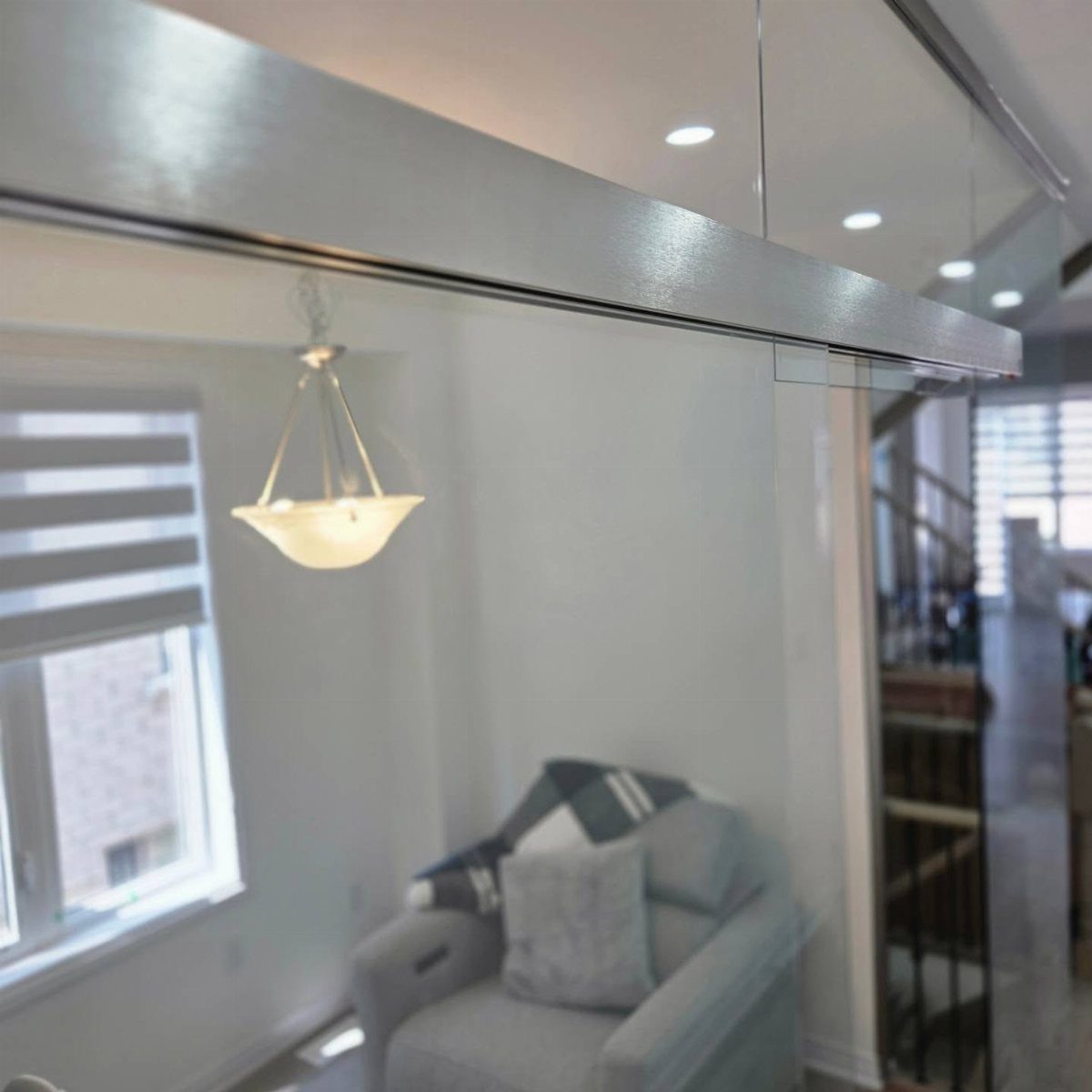 Glass partition with a silver metal frame separating a living room with a grey armchair.