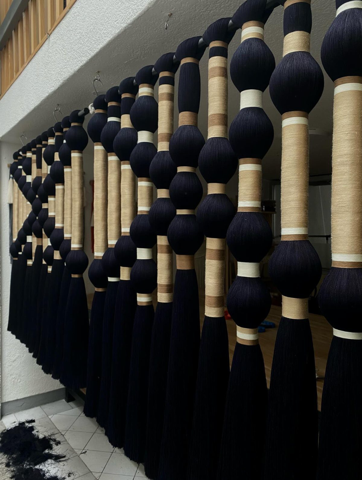Textured black and beige yarn dividers hanging vertically from a rod in a bright room.