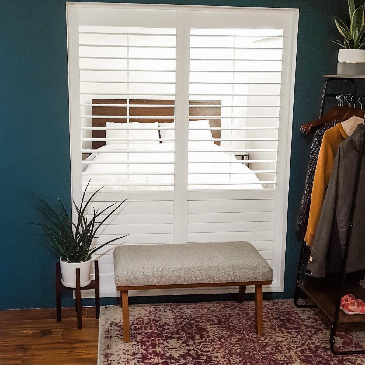 White plantation shutters dividing a living space from a bedroom with a white bed.