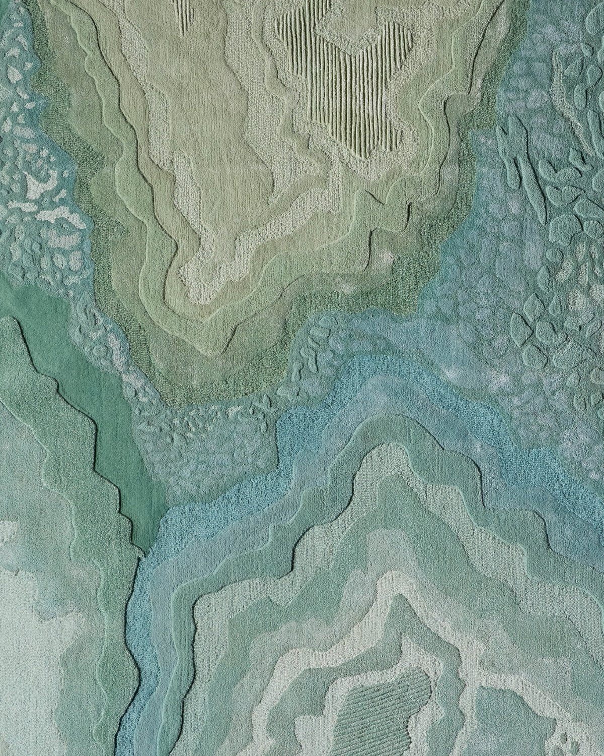 Textured abstract rug with topographical patterns in shades of green and blue.