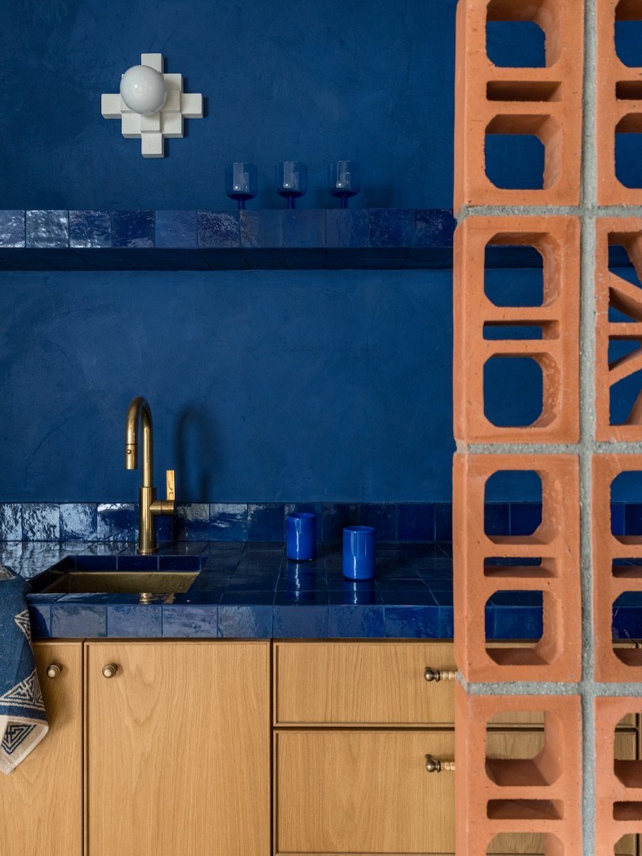 Terracotta hollow block partition separating a blue kitchen with wooden cabinets and gold fixtures.