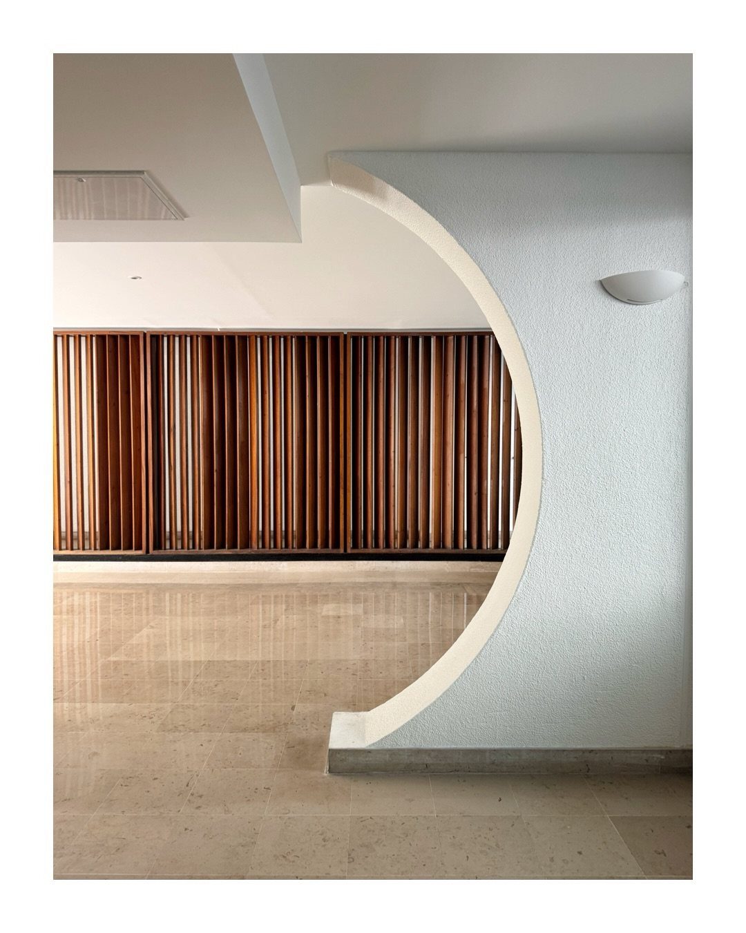 Circular wall opening revealing a wooden slat divider in a modern minimalist room.