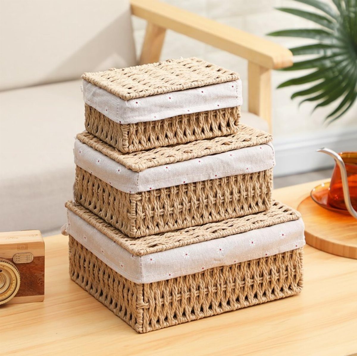 Three stacked woven wicker baskets with white fabric lids sitting on a wooden surface.