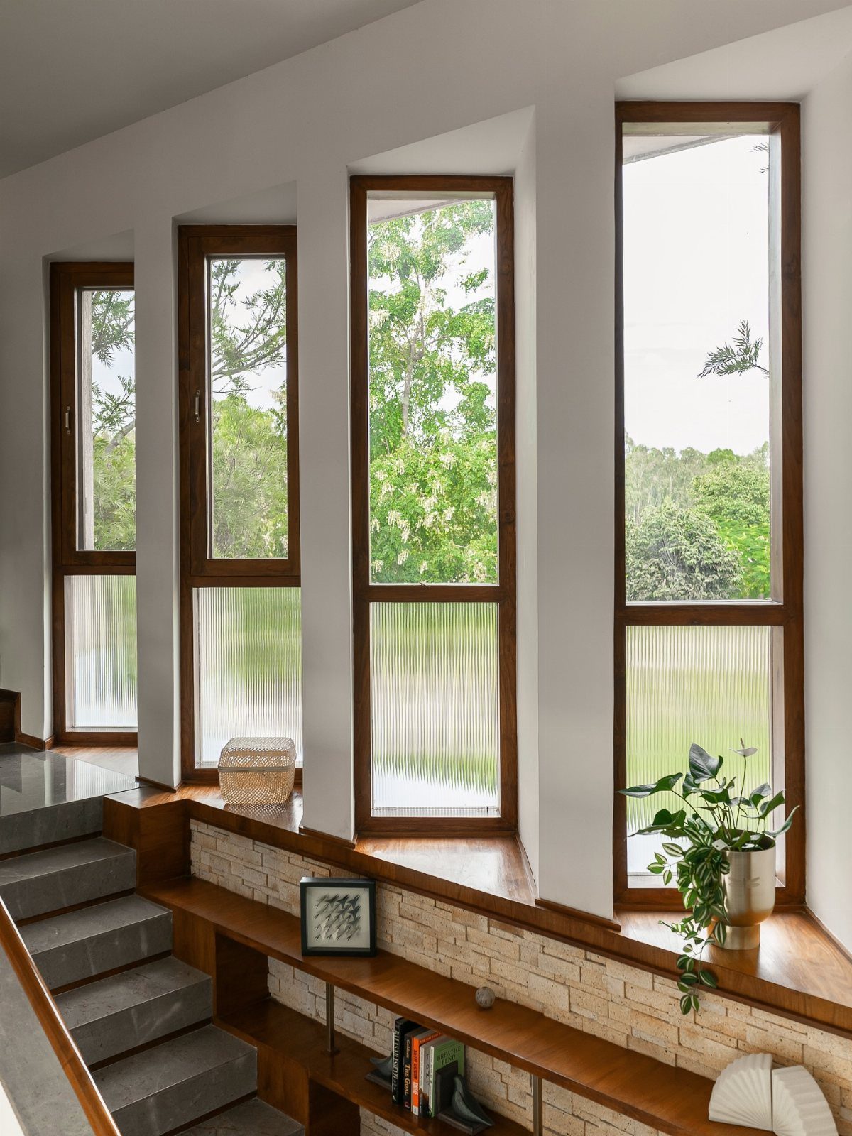Tall wooden-framed windows overlooking green trees, flooding a modern room with bright natural light.