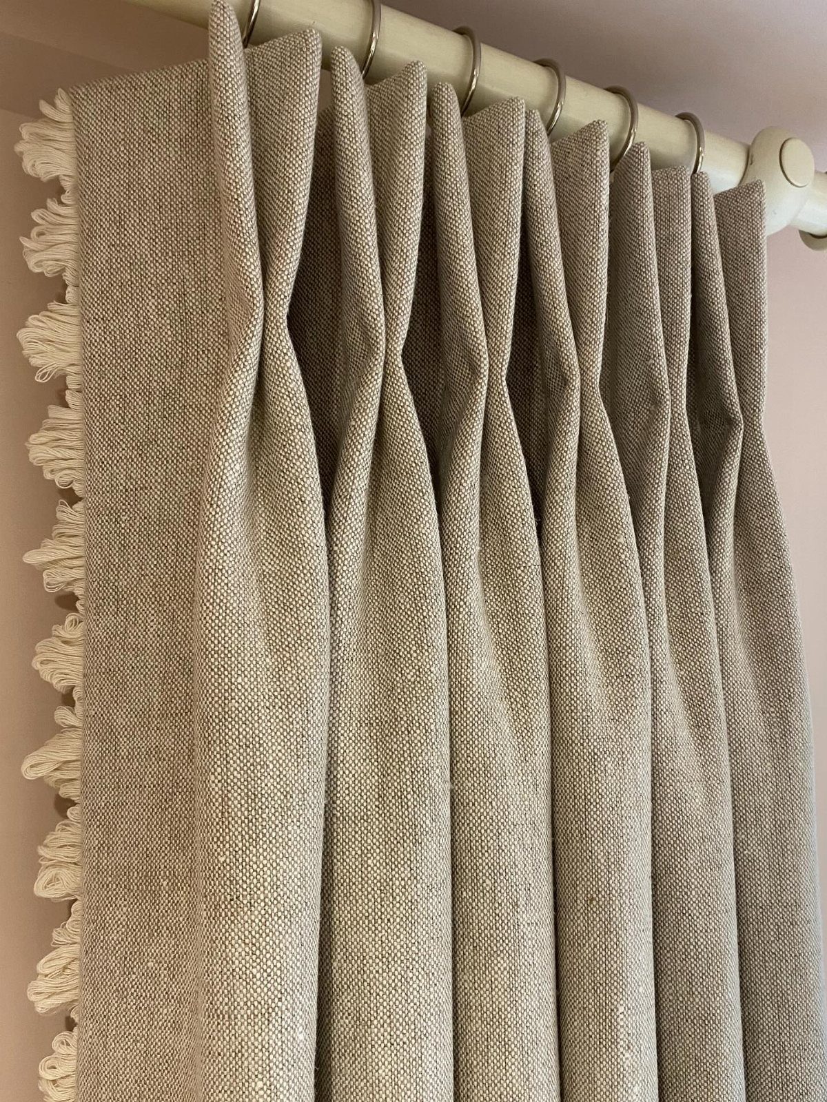 Textured beige linen curtains with tassel fringe hanging from a white curtain rod.