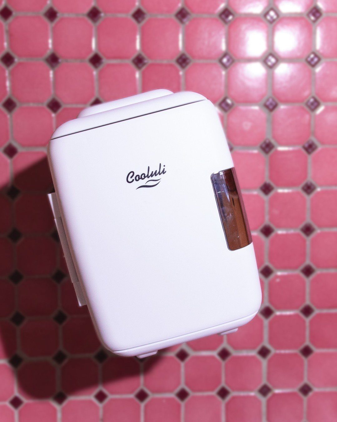 White Cooluli mini fridge resting on a pink tiled bathroom surface.