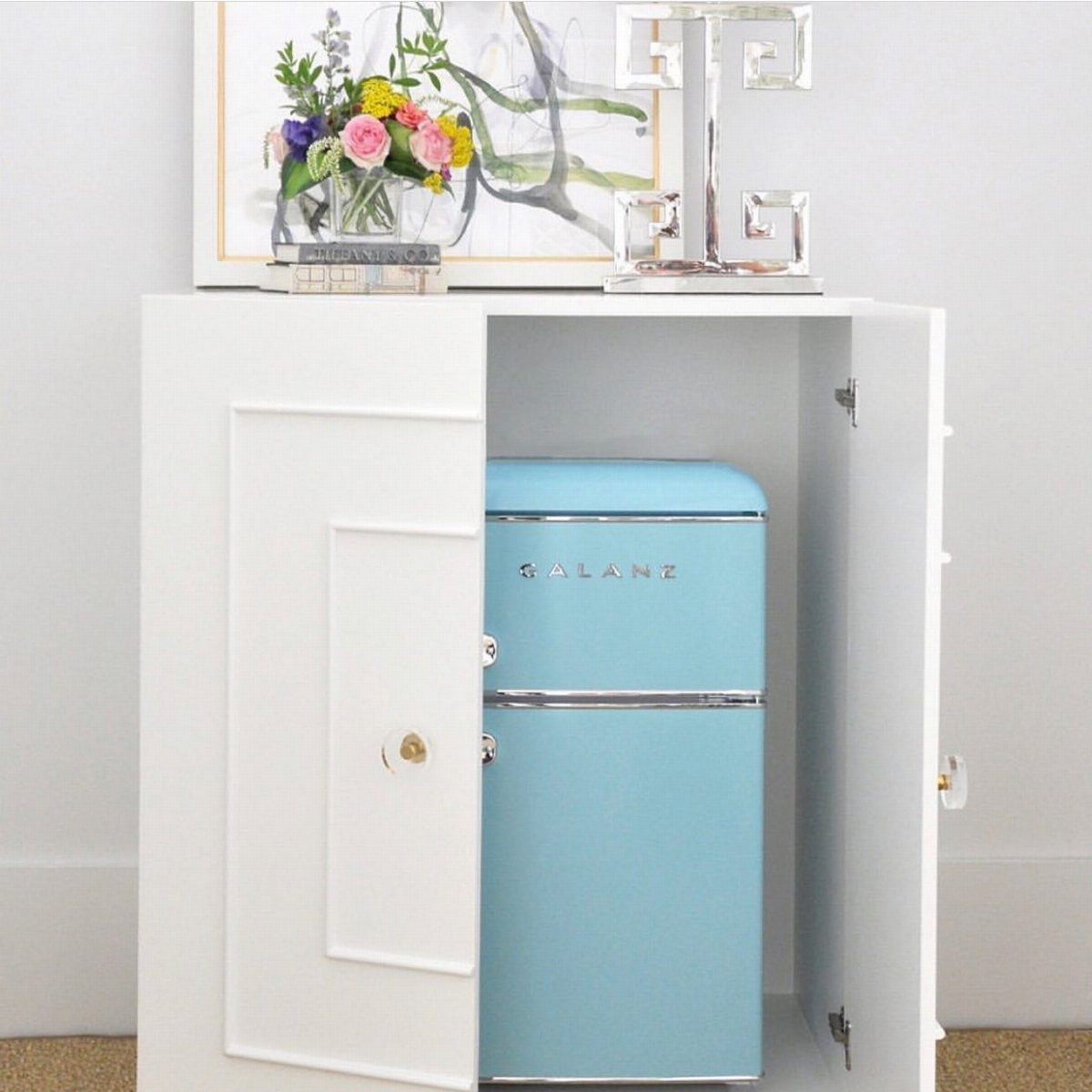 A light blue retro mini fridge tucked inside an open white cabinet console.