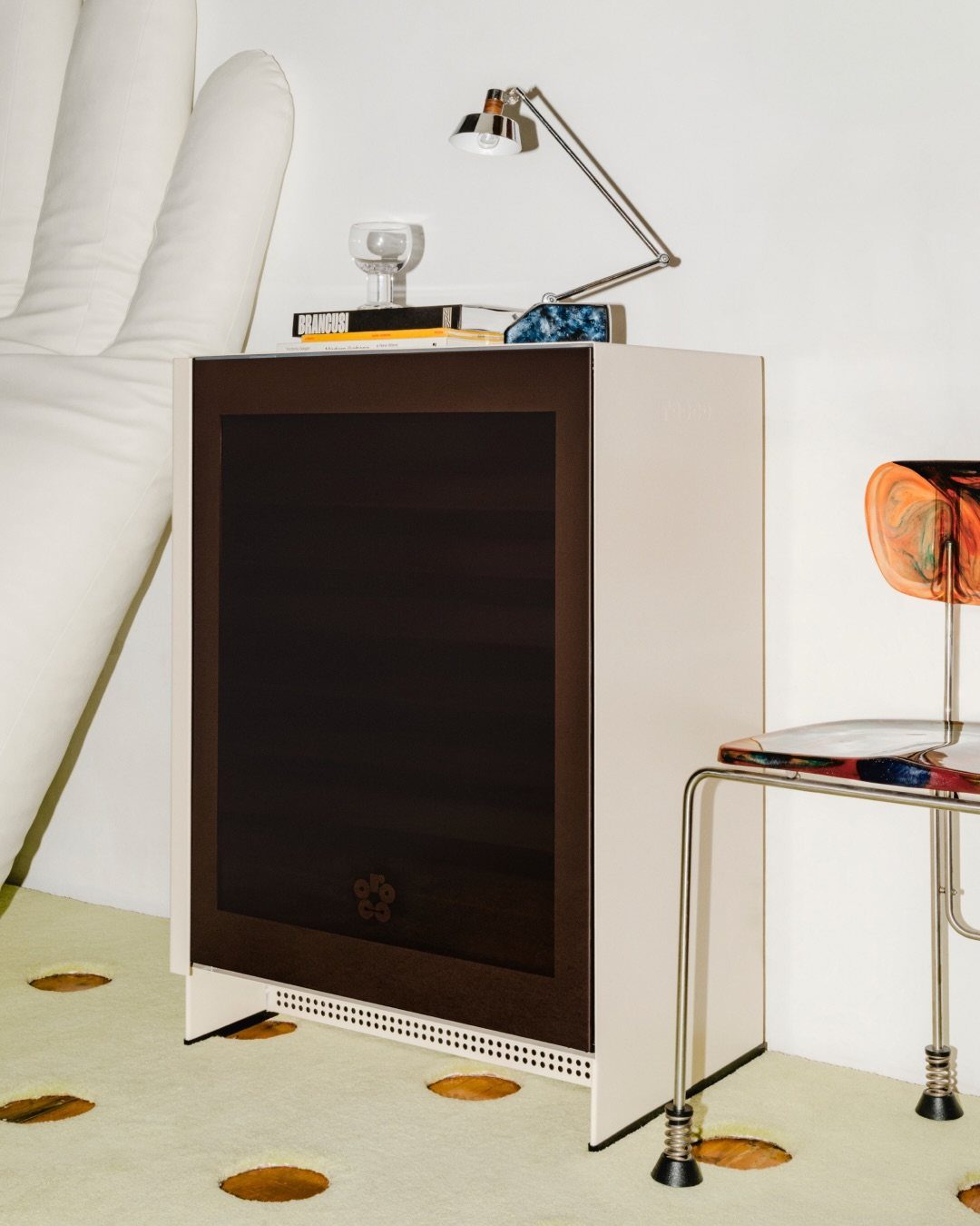 A cream mini fridge styled as a nightstand with a lamp and books on top.