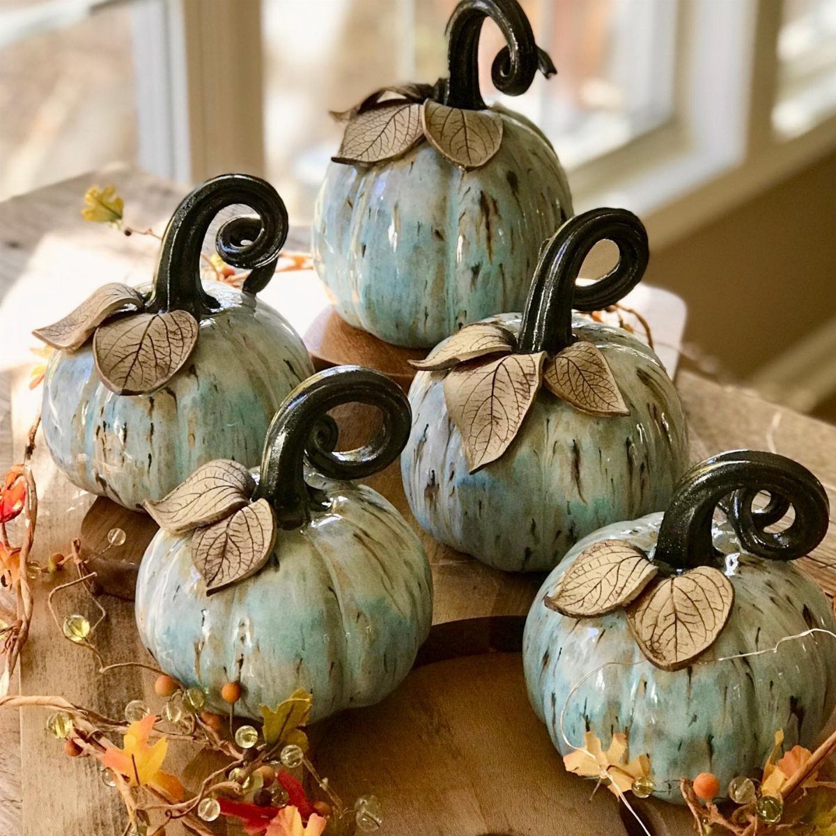 Five light blue watercolor-style ceramic pumpkins with dark curly stems and dried leaves.