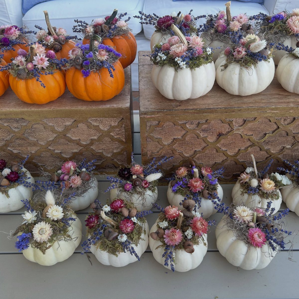 Mini orange and white pumpkins decorated with colorful dried floral arrangements on wooden boxes.