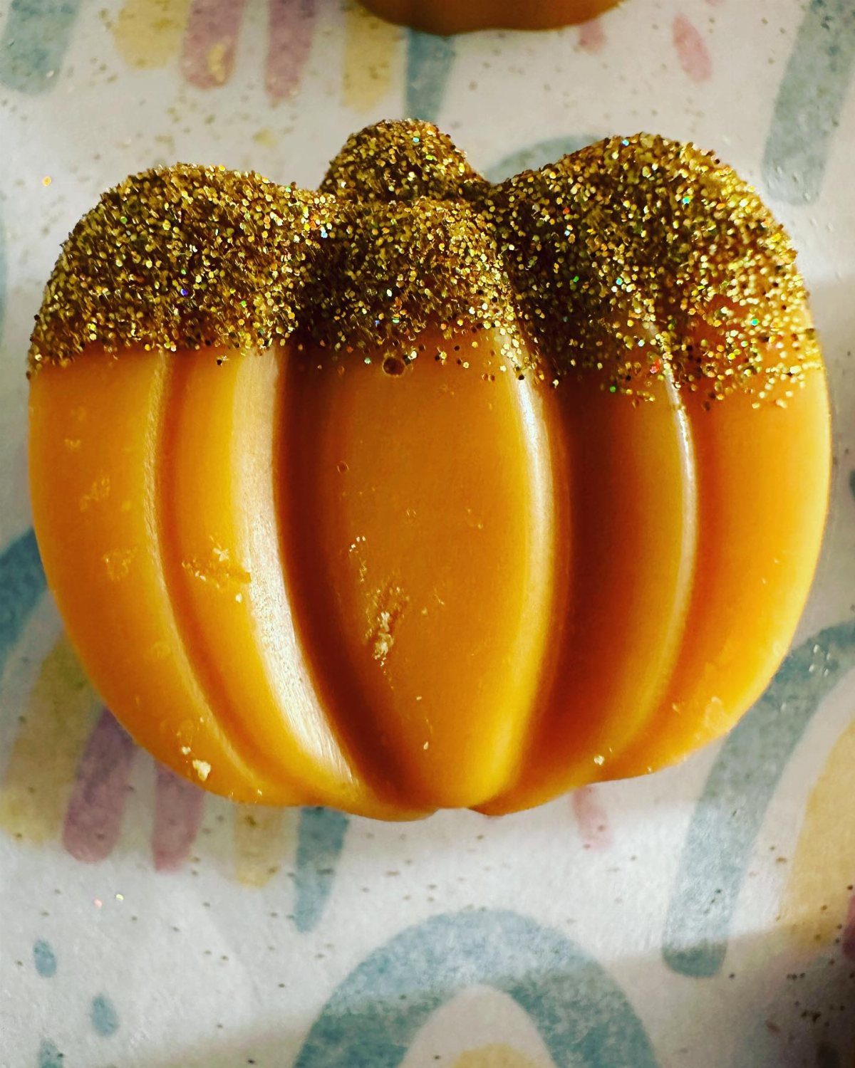 An orange pumpkin-shaped object decorated with sparkling gold glitter on its top half.