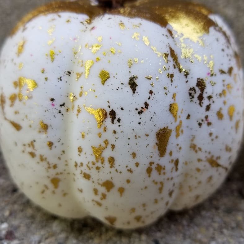 White mini pumpkin decorated with gold metallic splatters and flecks on a textured surface.