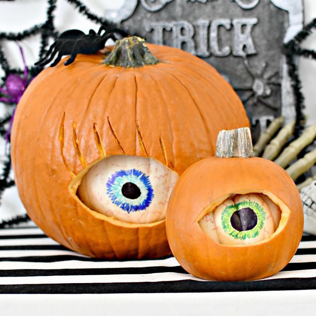 Two carved pumpkins with realistic eyeballs inside, set against spooky Halloween decorations.