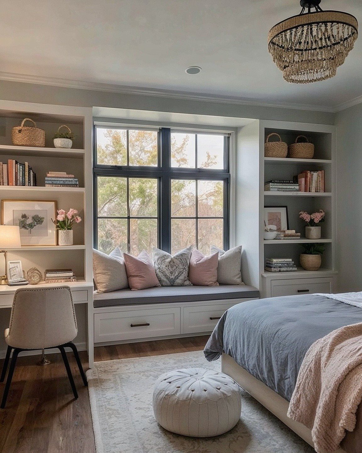 A built-in window seat with grey cushions and pink pillows sits between two white bookshelves.
