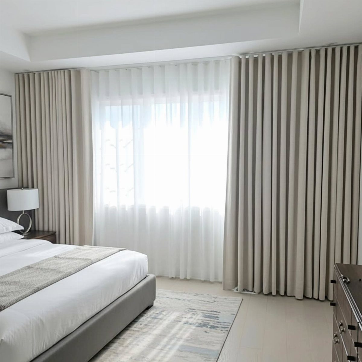 Beige floor-to-ceiling drapery and sheer white curtains covering a large window in a modern bedroom.