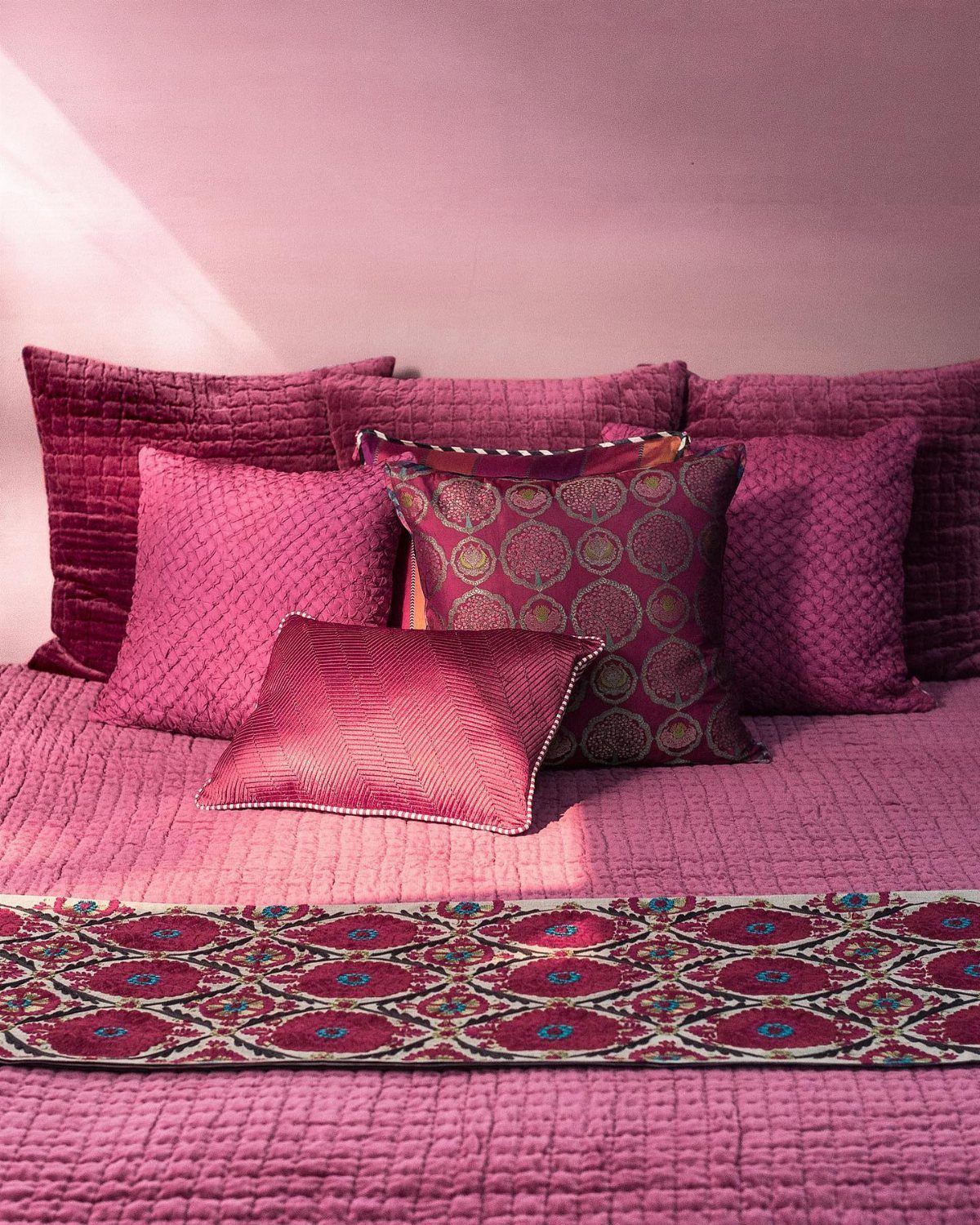 Pink quilted bedding with decorative magenta patterned pillows on a bed.