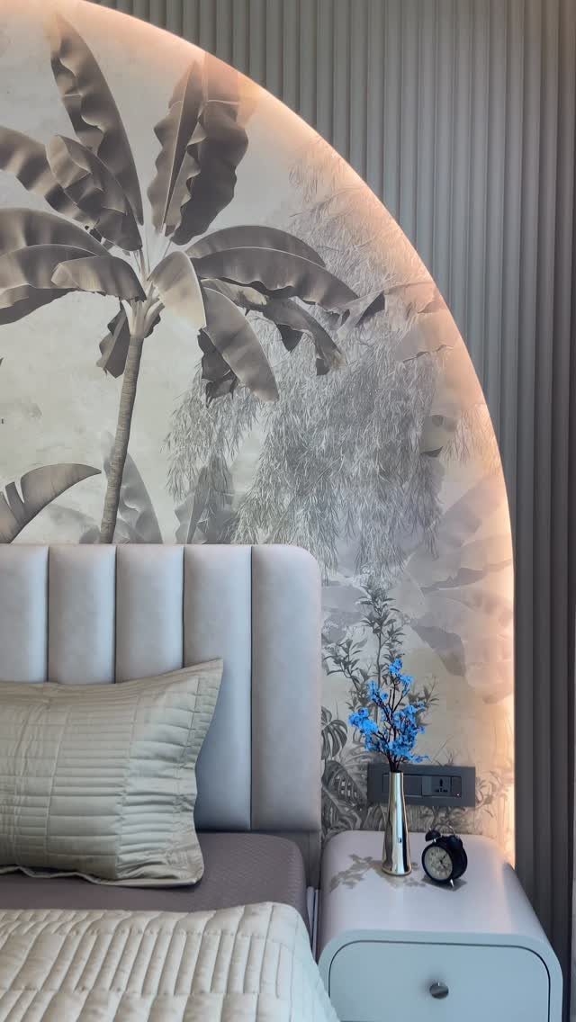 A bedroom with a large arched tropical mural behind a grey tufted headboard and white nightstand.