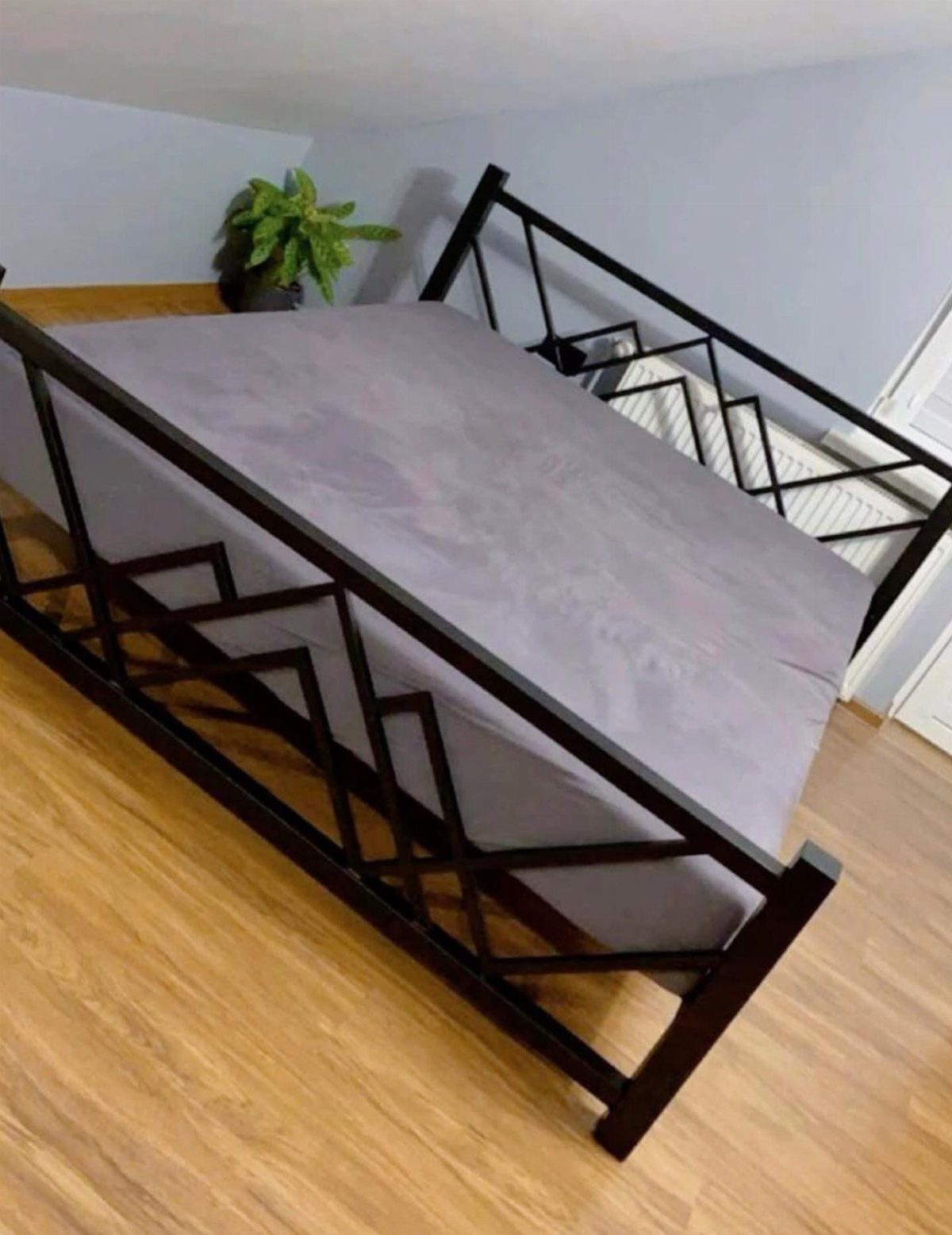 A black geometric metal bed frame with grey bedding on a wooden floor.