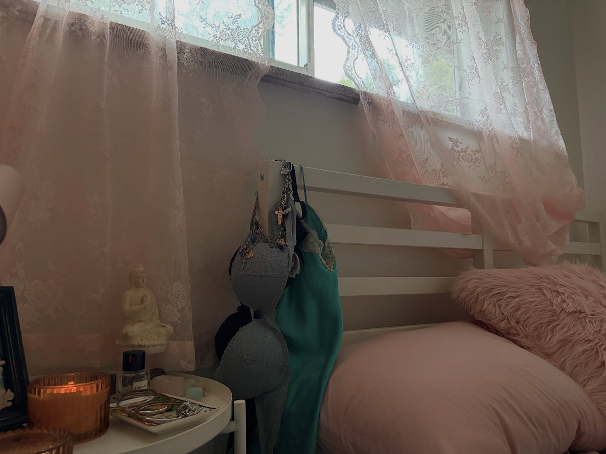 Pink bedding and lace curtains next to a white bed with a Buddha statue and candle.