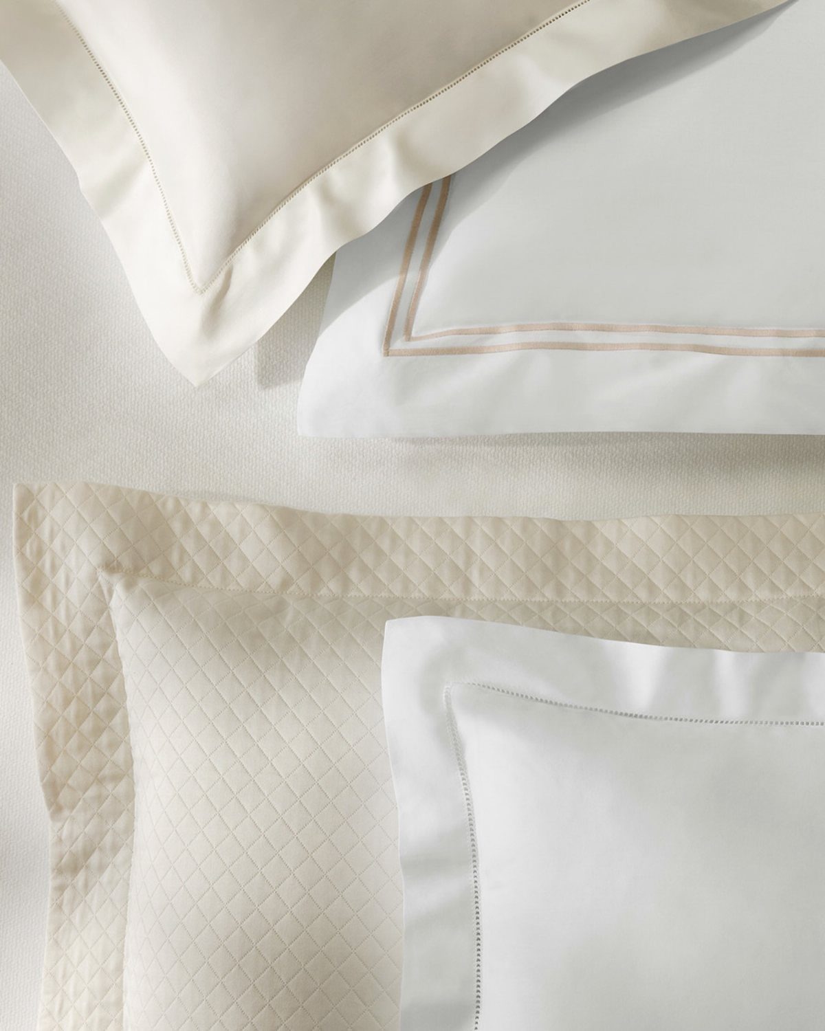 Cream and white pillows with quilted and smooth textures arranged on a bed.